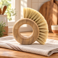 Harvest Ring Vegetable Brush hero: Harvest ring vegetable brush with pale bristles on a cream linen and oak counter